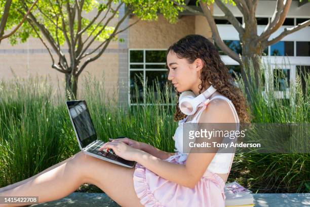 teenage girl sitting outside high school working on laptop - skirt stock photos et images de collection