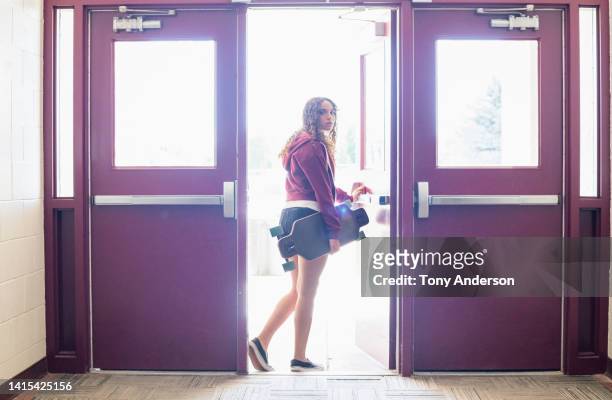 female high school student leaving building with her skateboard - highlights stock-fotos und bilder