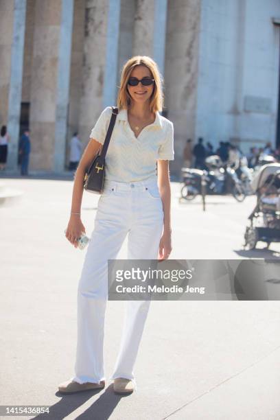 Model Chloe Lambert wears black sunglasses, a cream knit polo top tucked into high-waisted white jeans, brown suede Birkenstock sandals, and a small...