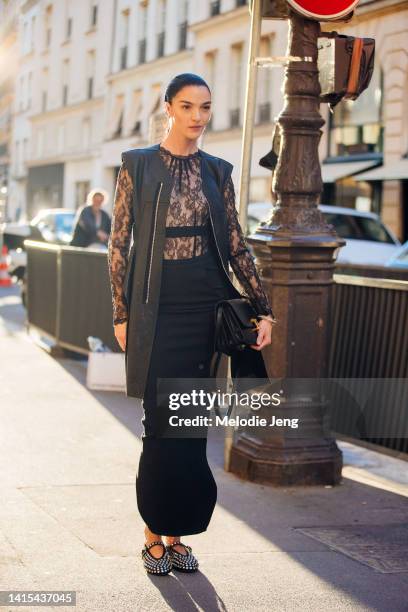 Model Mariacarla Boscono wears a long black skinny leather zip up vest, black lace top, high-waisted long maxi skirt, black leather purse, and black...