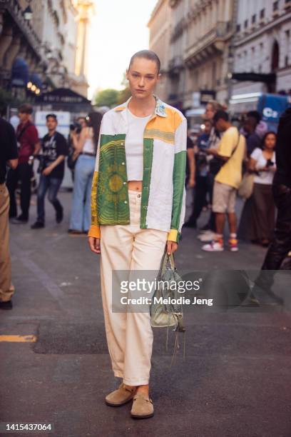 Model Ella Rattigan wears a green, yellow, and white patchwork napkin shirt, cream mid-rise jeans, brown Birkenstock clogs, and a Balenciaga moto bag...