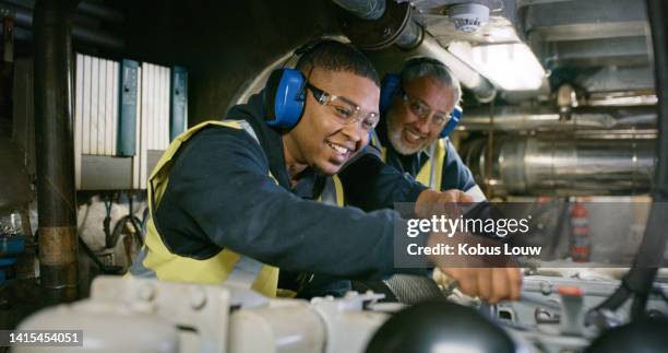 senior expert mechanic coaching a trainee in a manufacturing plant. smiling men in uniform working on engine repair in factory wearing safety glasses. professional mechanic in development - praktikant bildbanksfoton och bilder