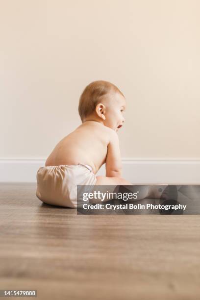 7 monate alter junge mit polydaktylenz, der eine neue entwicklungsfähigkeit erlernt, alleine zu sitzen, während er eine neutrale farbige wiederverwendbare stoffwindel trägt - babies only in cloth diapers stock-fotos und bilder