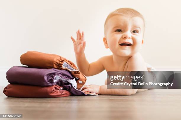 7-month-old baby boy wearing a neutral colored reusable cloth diaper laying on his belly & playing with his fall-colored cloth diapers - reusable diaper stock pictures, royalty-free photos & images