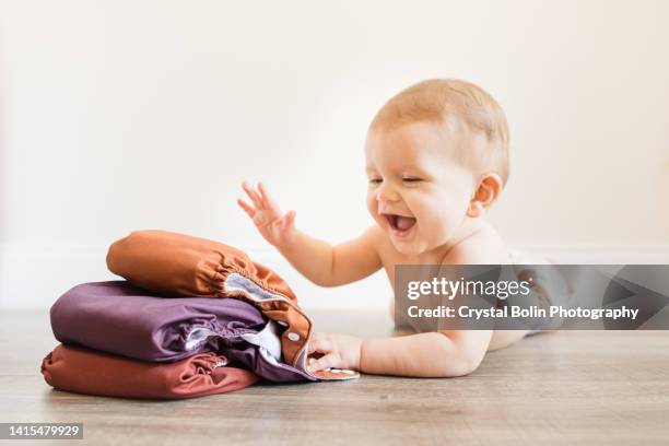 7-month-old baby boy wearing a neutral colored reusable cloth diaper laying on his belly & playing with his fall-colored cloth diapers - fralda de tecido imagens e fotografias de stock