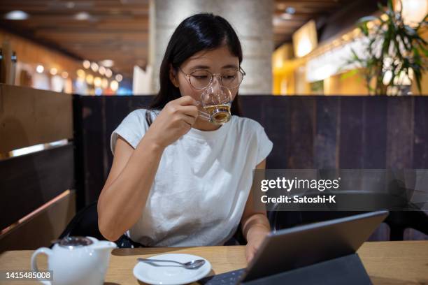 若い女性がカモミールティーを飲み、カフェでデジタルタブレットを使う - 若い女性一人 ストックフォトと画像