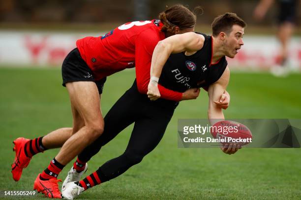 Zach Merrett of the Bombers handballs whilst being tackled by Harrison Jones of the Bombers during an Essendon Bombers AFL training session at The...