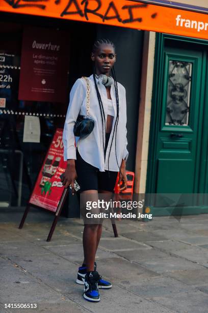 Nigerian model Divine Nwaokogba wears teal headphones, a small black leather shoulder bag, white shirt, white bandeau top, black biker shorts, and...