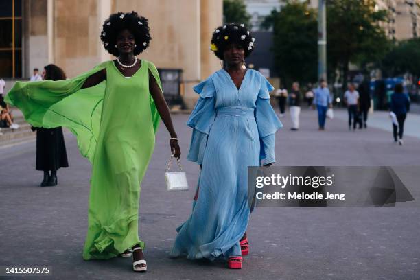 Two guests wear flowers in their afro hair, green and blue layered ruffle sleeve maxi dress dresses, white and red heels, and a pearl necklace...