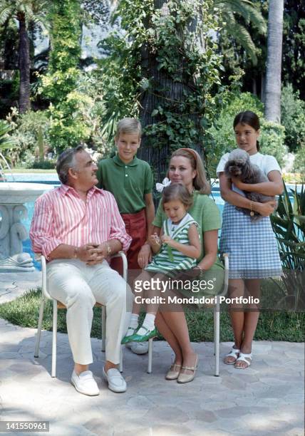 Prince Rainier III of Monaco sitting in a garden with his wife, the American actress Grace Kelly, and his children Albert, Caroline and...