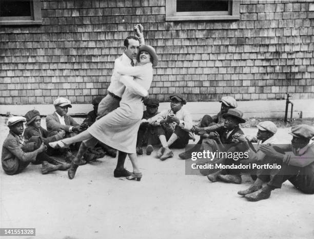 American dancers Marion and Martinez Randall performing a charleston step watched by some black children sitting on the ground. Palm Beach, 1920s