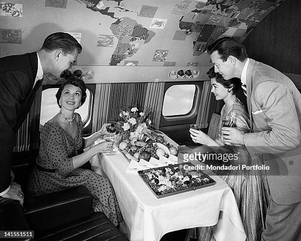 Two American women and two American men smiling in front of the buffet served on the intercontinental aeroplane 'Super G Constellation' of the...