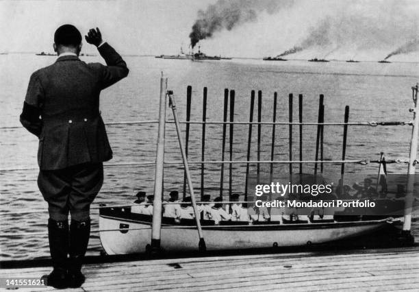 Fuhrer and Chancellor of Germany Adolf Hitler waving the ships on parade of the German Navy. Sailors in a lifeboat respond to the salute raising...