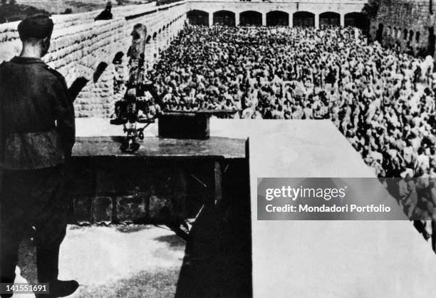 Soldier watching prisoners from an observation post of the Mauthausen-Gusen Concentration Camp, who are waiting for roll call completely naked....