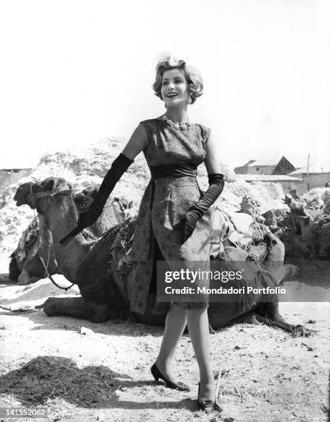 An Italian model wearing an evening dress in front of a dromedary. Italy, 1958