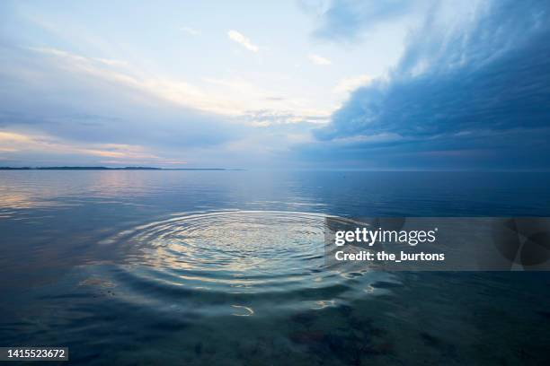 circular pattern on water surface by the sea, dramatic sky and dark clouds - dark ocean ripples stockfoto's en -beelden