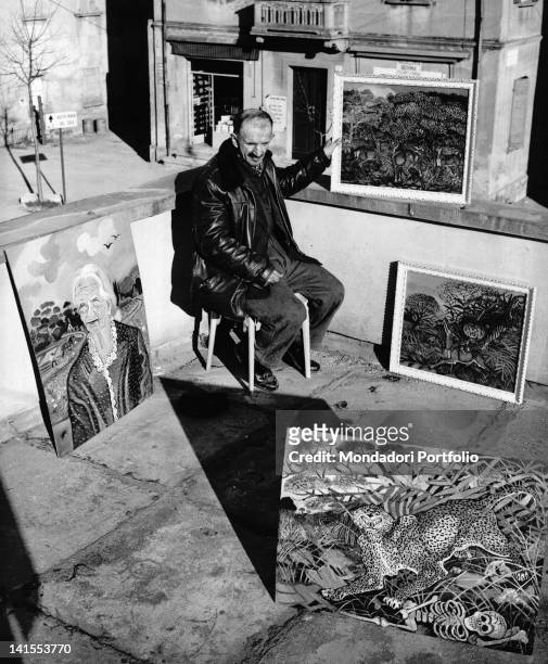 The Italian painter Antonio Ligabue sitting on the terrace of a friend with some of his paintings. Reggio Emilia, March 1961