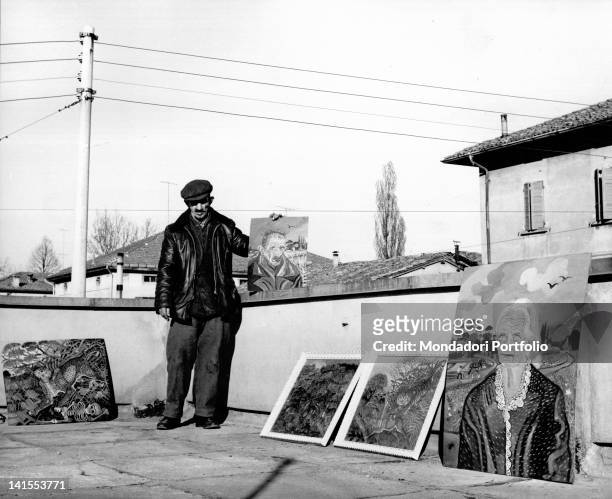 The Italian painter Antonio Ligabue posing on the terrace of a friend with some of his paintings. Reggio Emilia, March 1961