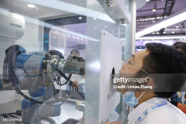 Staff member takes part in a demonstration of a robot arm collecting swab samples for coronavirus disease detection during the 2022 World Robot...