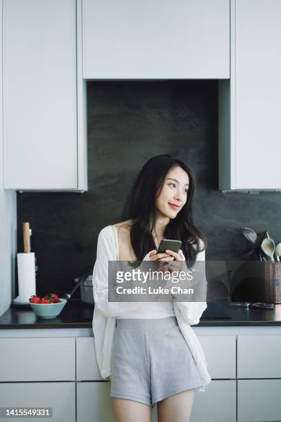 asian beautiful woman using smartphone at home - woman drinking phone kitchen stockfoto's en -beelden