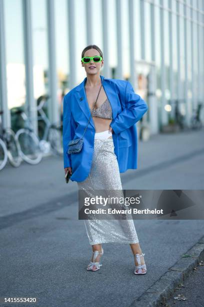 Guest wears neon green sunglasses, a blue oversized blazer jacket, a silver rhinestones V-neck / cropped top, a blue denim ripped crossbody bag from...