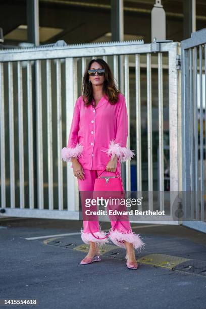 Guest wears black sunglasses, silver earrings, a pink oversized silk buttoned shirt with pale pink embroidered feathers, matching neon pink suit...