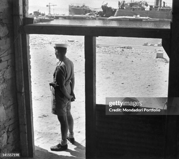 British marine sentry standing guard outside the headquarters of the Admiralty in Tobruk, in the background is a ship wreck. Tobruk, June 1941