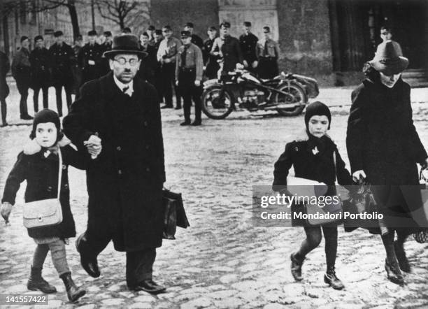 Jewish family receiving insults and invectives from of a group of brownshirts; the girls already have special symbols on their coats that distinguish...