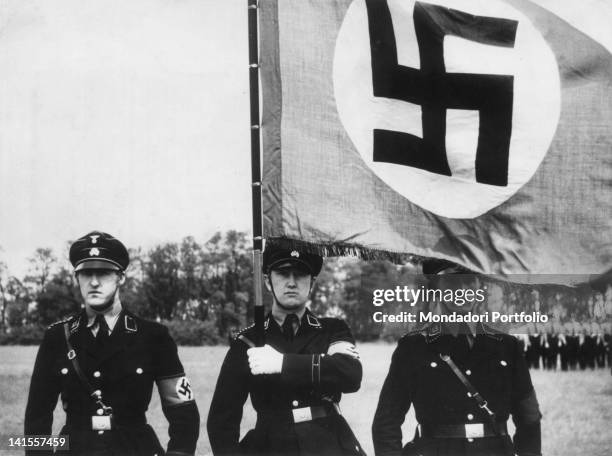 Three members of the German SS with the Nazi flag at a military parade in Munich. Munich, 1926