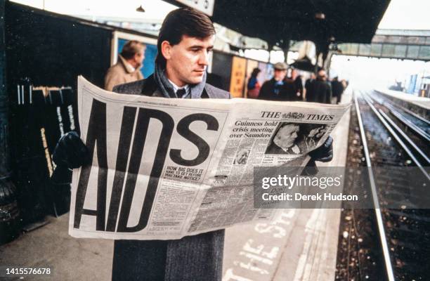 An unidentified commuter reads a copy of the Times newspaper, which features an AIDS awareness campaign advertisement, as he stands on a train...