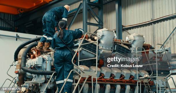 engineer and mechanic working together as a team to fix, repair or maintain a large engine inside of a factory or production warehouse. technician and shipwright doing a service on a machine part - electric motor stock pictures, royalty-free photos & images