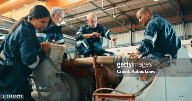 group of mechanical engineers fixing, repairing or performing maintenance check on heavy industrial machinery in production factory. diverse team of workshop technicians or mechanics working together - coveralls stock pictures, royalty-free photos & images