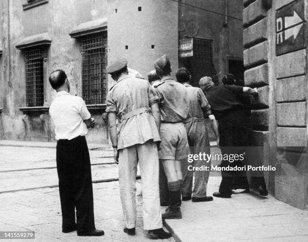 Canadian soldiers and Italian civilians hidden behind a house observing a fight between partisans and fascist snipers during the liberation of the...