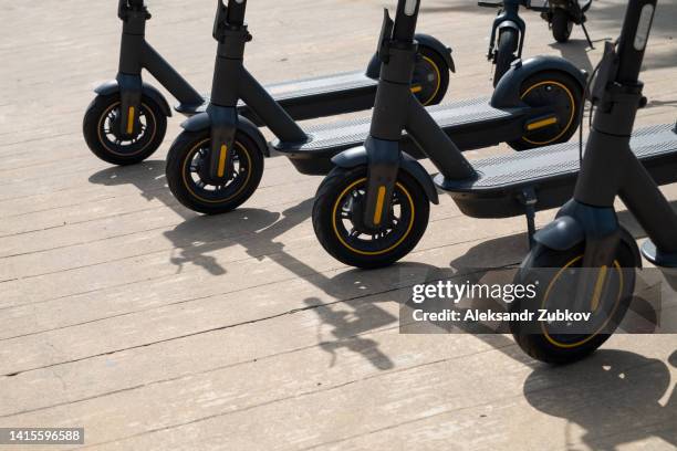 electric scooters stand in a row, for commuting, for recreation. environmentally friendly transport, outdoors. a modern way of getting around on city streets. eco-friendly mode of transport. environmental protection. active and healthy lifestyle. - trotinete imagens e fotografias de stock