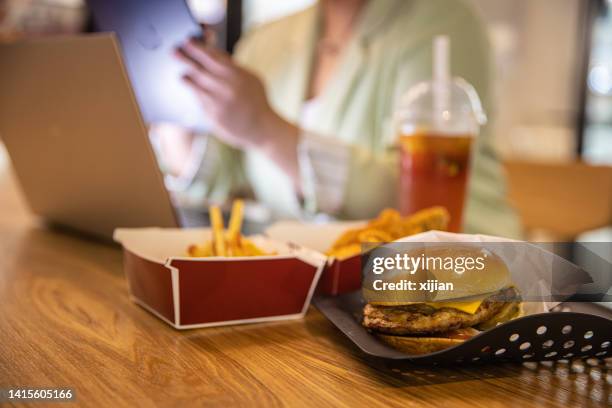 mujer de negocios trabajando en una computadora portátil con comida rápida en la mesa del restaurante - comida rápida fotografías e imágenes de stock