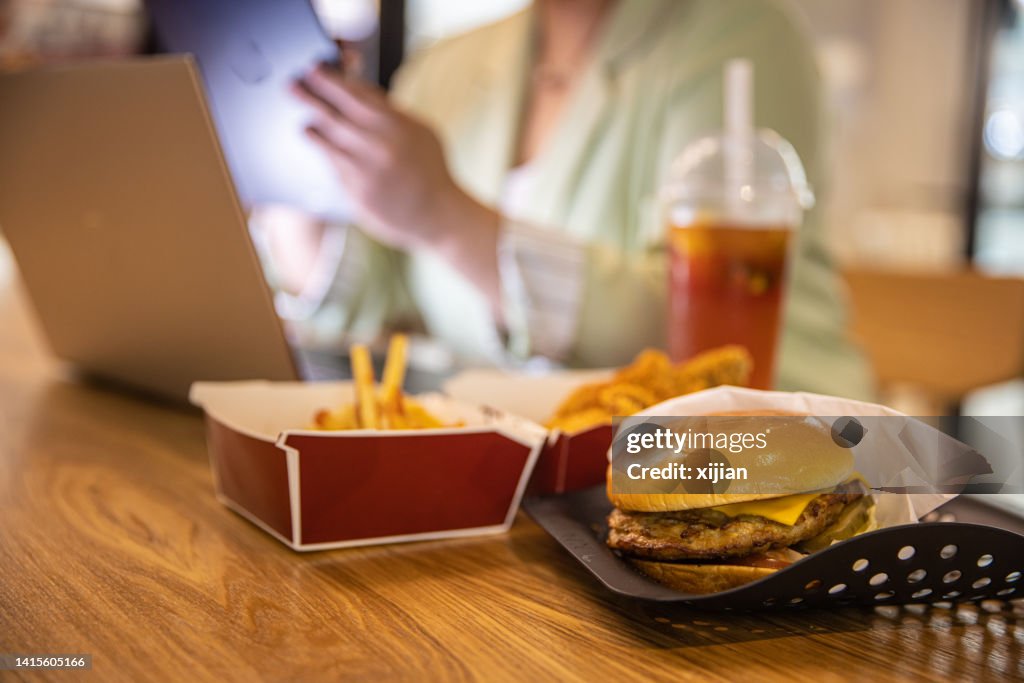Empresária trabalhando no laptop com fast food na mesa de restaurante