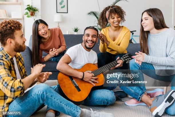 young group of diverse friends social gathering having fun together while singing and playing the guitar at home. friendship, home entertainment and people concept - acoustic guitar foto e immagini stock