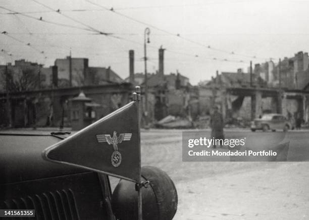 Close-up of the flag on a car belonging to the German General Staff. On the background, the ruins of the Spomenik square in Belgrade. Yugoslavia, on...