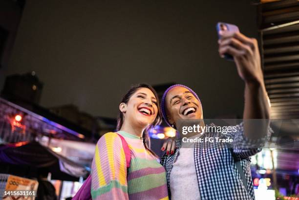 young couple (or friends) taking selfies or filming using mobile phone outdoors at festival by the night - including a transgender person - spectator selfie stock pictures, royalty-free photos & images