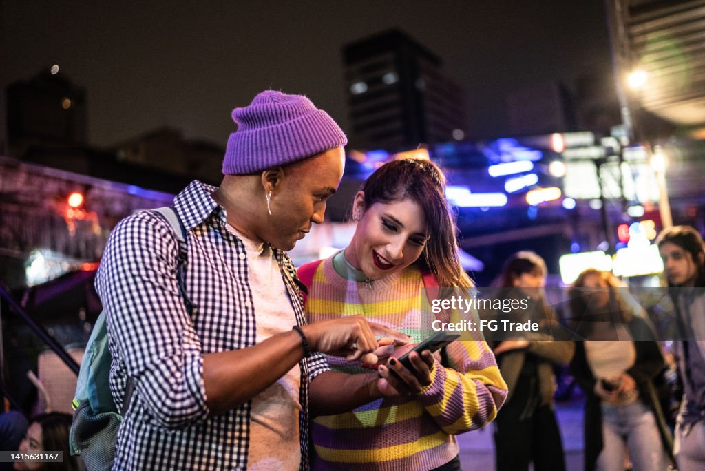 Young couple (or friends) using mobile phone at festival by the night - including a transgender person