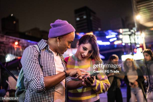 young couple (or friends) using mobile phone at festival by the night - including a transgender person - music festival phone stock pictures, royalty-free photos & images