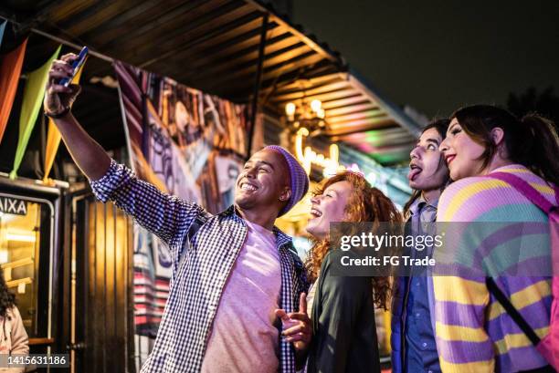 amigos que se toman selfies o filman con un teléfono móvil al aire libre en el festival por la noche, incluida una persona transgénero - festival de cine fotografías e imágenes de stock