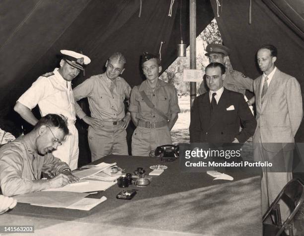 In the headquarters tent, the diplomatic and military authorities are signing the armistice between Italy and the Alllied Forces. From the left, the...