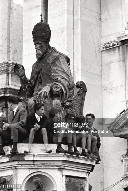 Some boys are sat down on the base of the statue of Sixtus V, in front of the Basilica of Loreto; they are waiting for the arrival of Pope John...