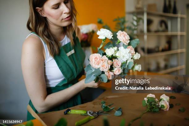 pretty young woman florist with long hair collects a bouquet of flowers in eco style. - magasin de fleurs photos et images de collection