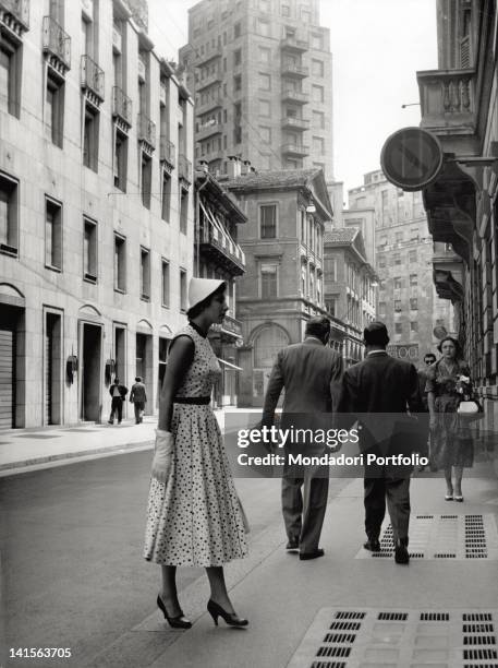 An elegantly dressed girl is looking at a window shop in via Monte Napoleone. Milan, the '50s.