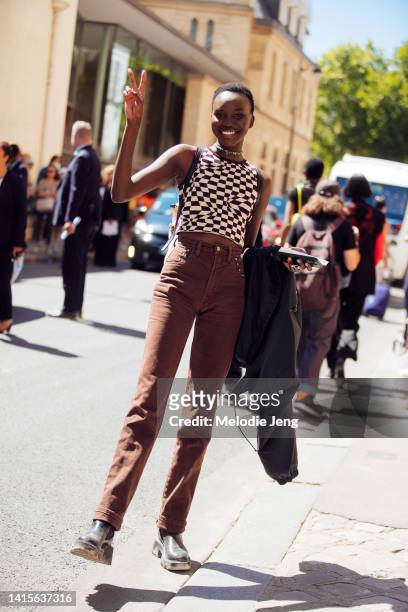 Model Achenrin Madit throws a peace sign and wears a green choker 90's style stone necklace brown and white checkered psychedelic style Y2K tank cop,...