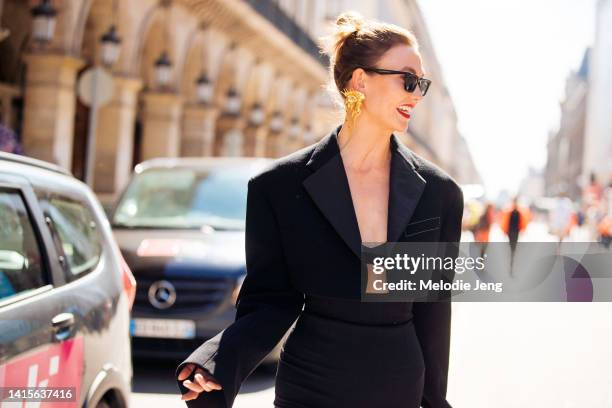 Model and entrepeneur Karlie Kloss wears black sunglasses, red lipstick, a large gold Schiaparelli earring, a black crop high shoulder blazer top,...