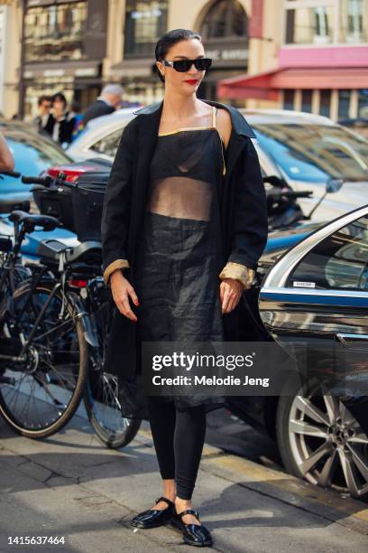 Model Mariacarla Boscono wears a black Burberry trench coat, sheet black dress covering with a gold lining, black bra top, black leggings, black...