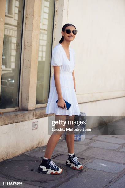 Model Mariana Barcelos wears black sunglasses, a white lace insert v neck summer dress with balloon sleeves, blue and white Christian Dior cotton...